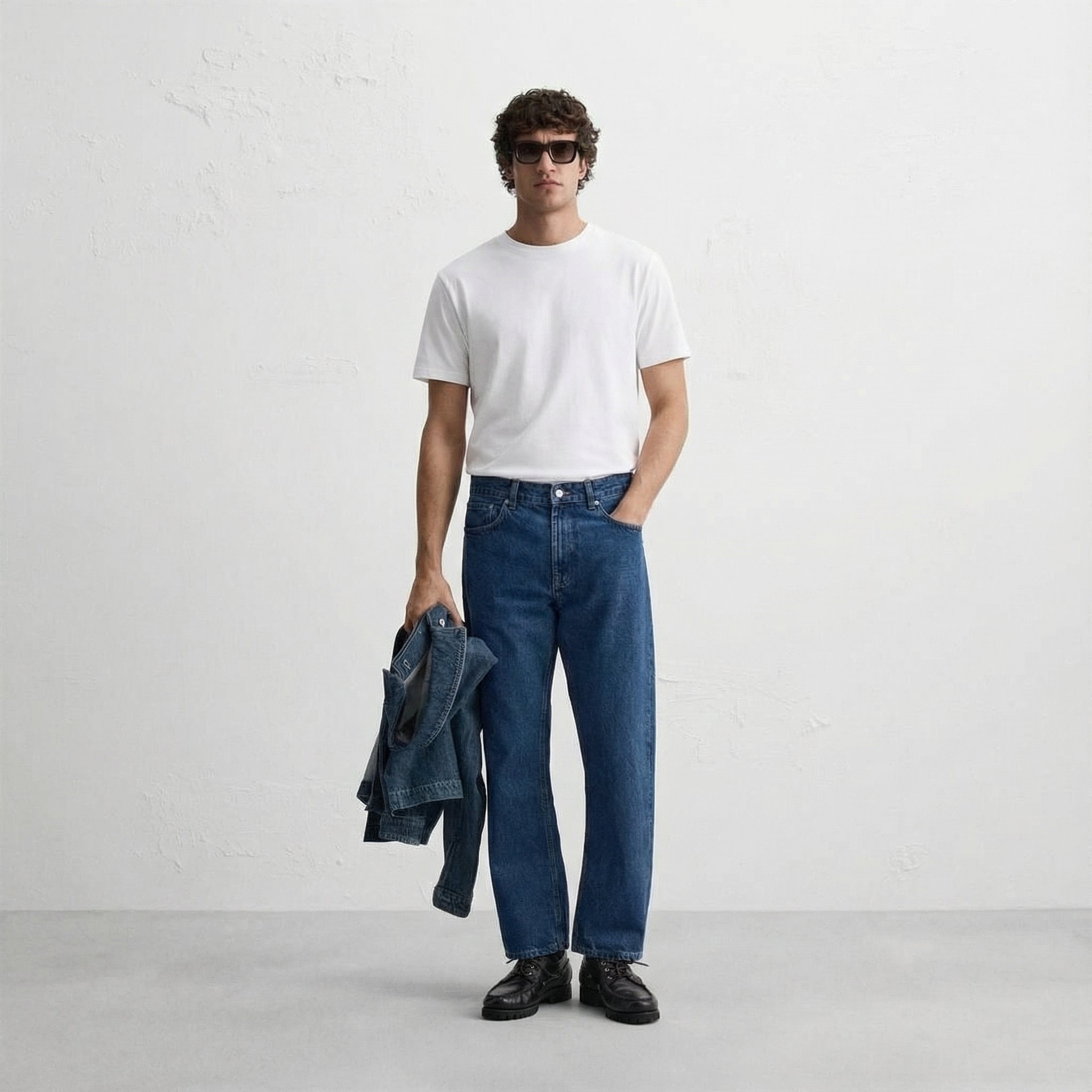 Man wearing a white t-shirt, blue jeans, and sunglasses against a plain background