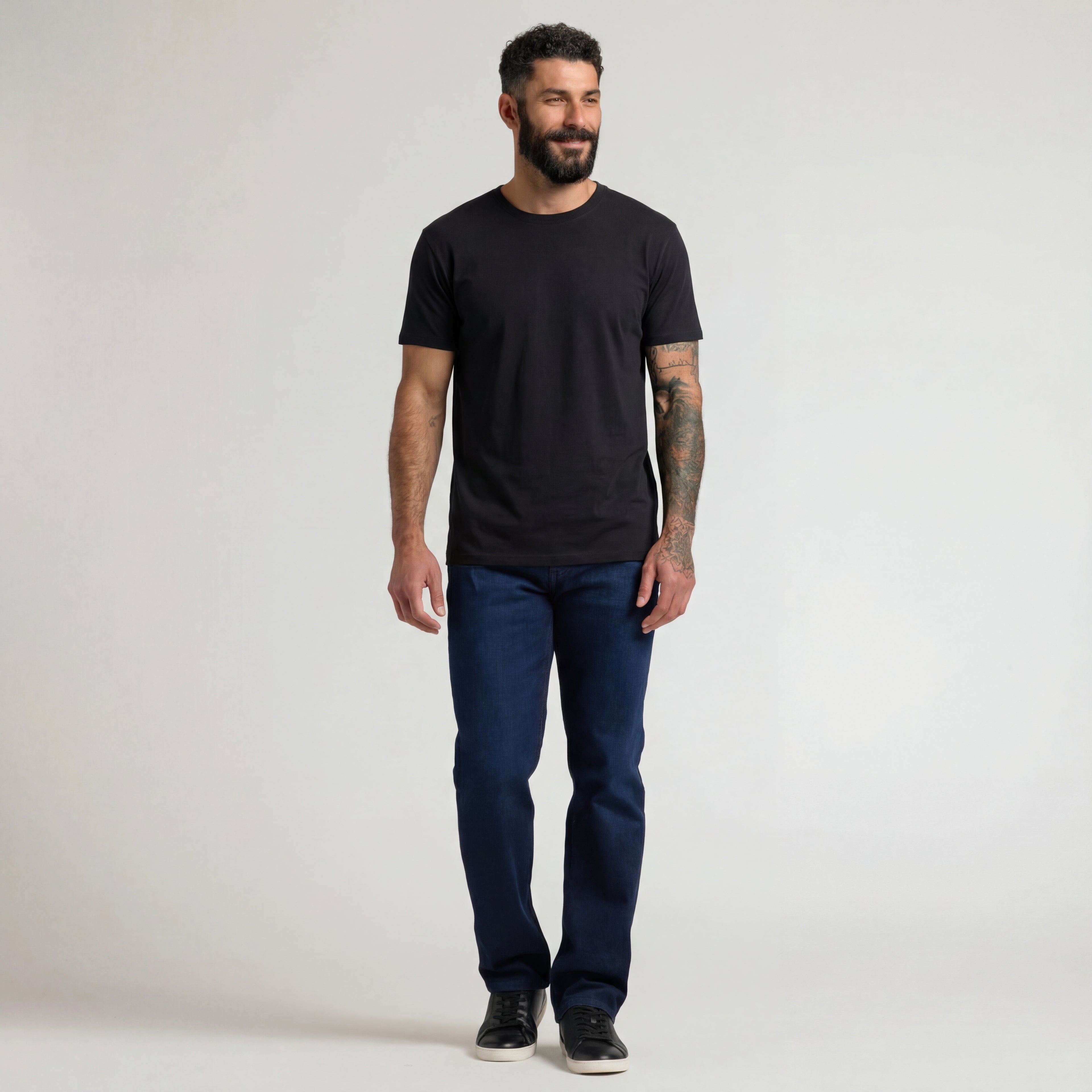 Man wearing a black t-shirt and blue jeans against a plain background